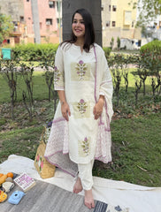 Woman in a white embroidered outfit sitting on a blanket outdoors with a basket and snacks.