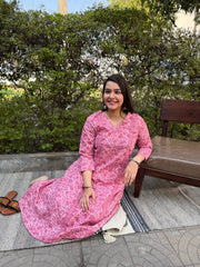 Woman in a pink dress sitting outdoors with greenery in the background