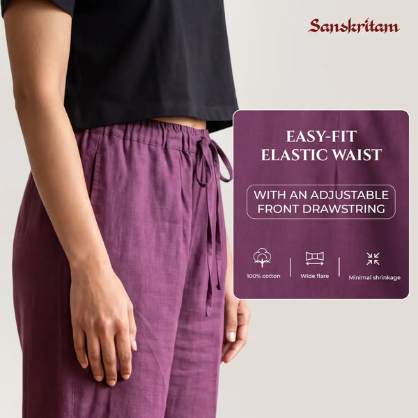 A person wearing purple drawstring wide-leg pants with a black cropped top, shown against a light gray background with a product feature panel and the Sanskritam brand name.